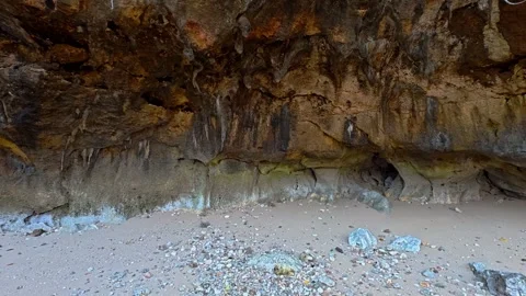 Weathered coastal cave wall above pale pebbled beach and rugged rock formatio Stock Footage 346741548
