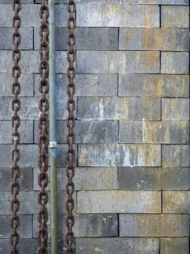 Weathered concrete block wall with rusty metal chains and industrial pipe, .. Stock Photos