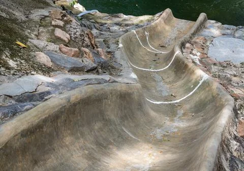 A weathered concrete slide winds like a smooth, gray ribbon down the rugged e Foto stock
