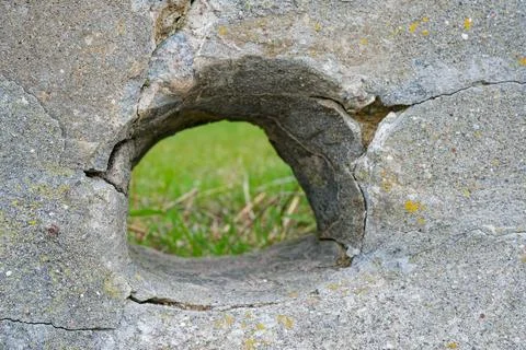 Weathered concrete wall with a circular hole showing green grass background Stock Photos