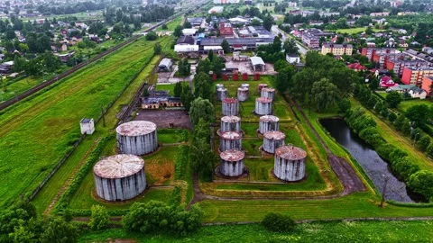 Weathered Cylindrical Storage Tanks Between Railway and Tree-Lined Canal, Aerial 動画素材 348899249