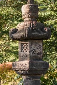 A weathered, dark gray stone lantern with carved details in a lush garden s.. Stock Photos