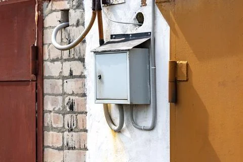 A Weathered Electrical Box Mounted on a Wall with Various Cables and Pipes in Stock Photos