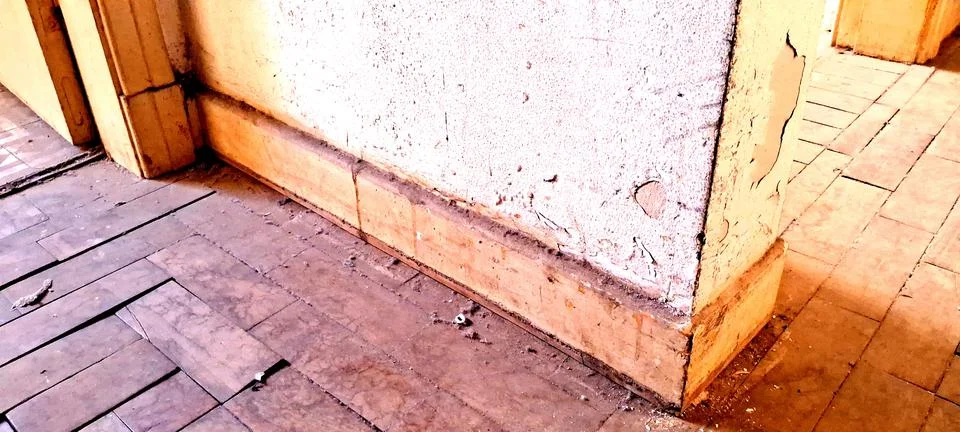 Weathered interior wall corner featuring cracked plaster and wooden baseboards Stock Photos