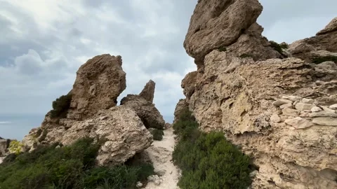 Weathered limestone rock pinnacles rise beside a coastal footpath honeycomb Видео 343679285