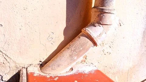 Weathered metal drain pipe attached to a cracked beige stucco wall Stock Photos