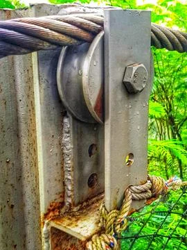 A weathered metal pulley system featuring a steel cable and knotted rope agai Stock Photos