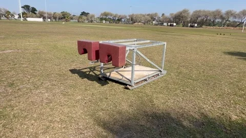 : A weathered metal rugby scrum machine with red padded sled sits idle on a Stock Footage 342483786