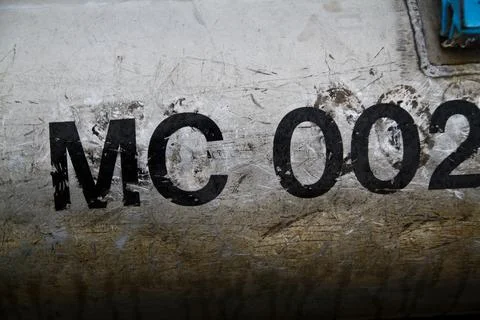 Weathered Metallic Surface with Stenciled Code MC 002 Close-Up Stock Photos