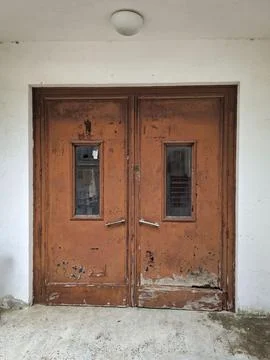 Weathered orange double door with small windows in abandoned hospital wall Stock Photos