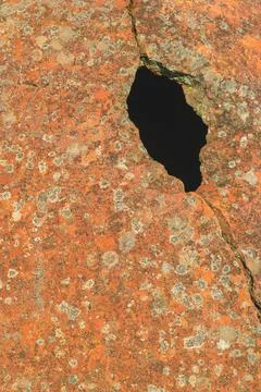 Weathered orange rock surface with irregular dark hole showing natural eros.. Stock Photos