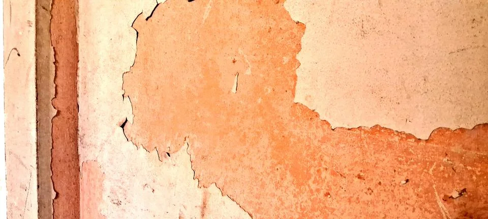 Weathered orange wall surface showing peeling paint and textured plaster layers Stock Photos