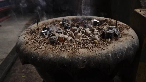 Weathered outdoor incense burner with burning sticks rising smoke small clay Stock Footage 345333232