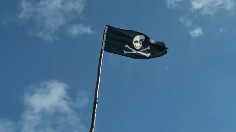 A weathered pirate flag flutters in the wind against a bright blue sky Stock Footage 285187820