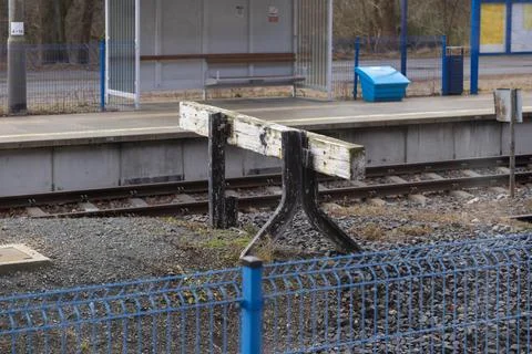 A weathered railway buffer stop stands at the end of train tracks near a modern 스톡 사진