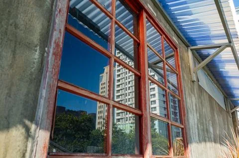 Weathered red window frames reflect modern skyscrapers against blue sky. 스톡 사진
