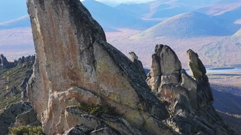 Weathered rock formations with moss and distant lake under shifting sunlight Stock Footage 346279335