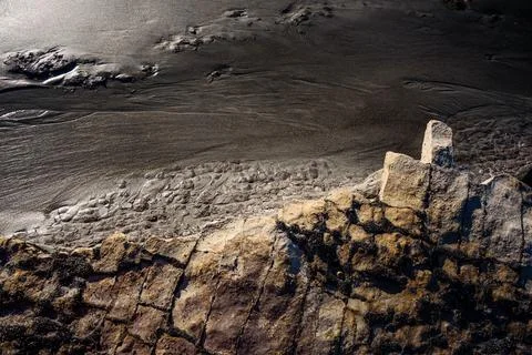 Weathered sandstone forms and dark sand contrast at a coastline in New Zealand Stock Photos