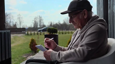 Weathered senior writing contemplative notes on wooden porch, reflecting amid Vidéo 306925755