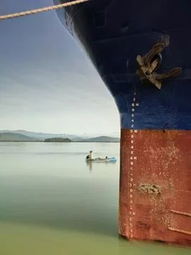 Weathered ship hull with draft marks docked in calm water, mountain backdrop 스톡 사진