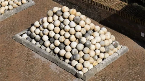 Weathered stone cannonballs form precise pyramid patterned brick paving within Stock Footage 326354634