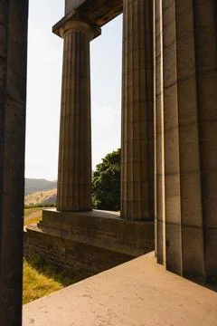 Weathered stone columns framing sunlit hills at Edinburgh classical monument Stock Photos