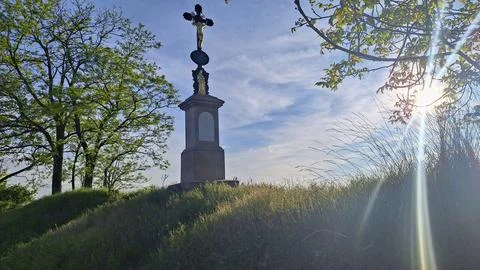 A weathered stone monument featuring a crucifix is bathed in the warm glow .. Stock Photos