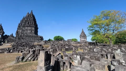 Weathered stone ruins fill the foreground beneath a Prambanan Temple tower .. Video stock 341542795