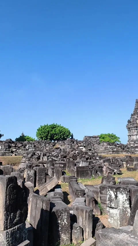 Weathered stone ruins fill the foreground beneath a Prambanan Temple tower .. Stock Footage 341543581
