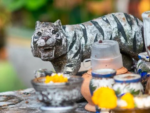 Weathered Stone Tiger Statue at Thai Outdoor Shrine with Flower Offerings a.. 스톡 사진