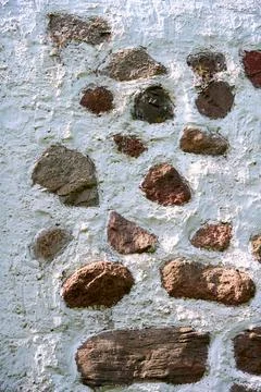 Weathered stone wall with embedded rocks and faded blue texture Stock Photos