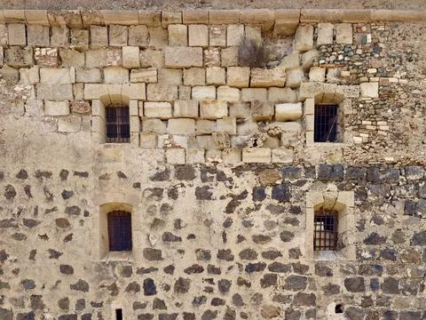 Weathered stone wall with small barred windows, mixed masonry textures, ero.. Stock Photos