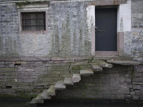 A weathered stone wall with steps over green water, China Stock Photos