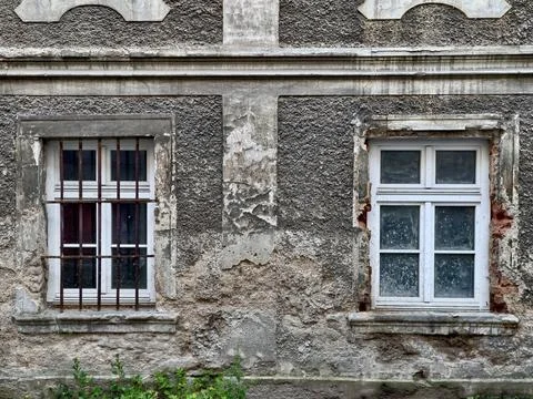 Weathered stucco facade with two old sash windows, iron bars, peeling paint.. Stock Photos