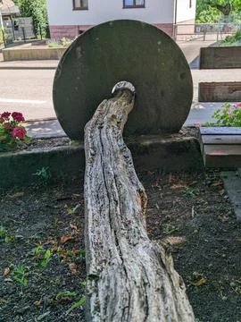 Weathered tree trunk threaded through a large circular stone wheel in a vil.. Stock-Fotos