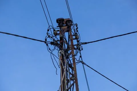 A weathered utility pole supporting complex electrical wiring against a clear Stock Photos