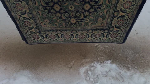 Weathered vintage rug draped over dusty floor with distressed floral design and Stock Footage 327417339