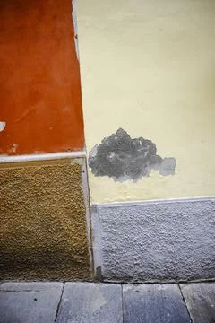 A weathered wall displays a striking patchwork of orange, yellow, gray, and Foto stock