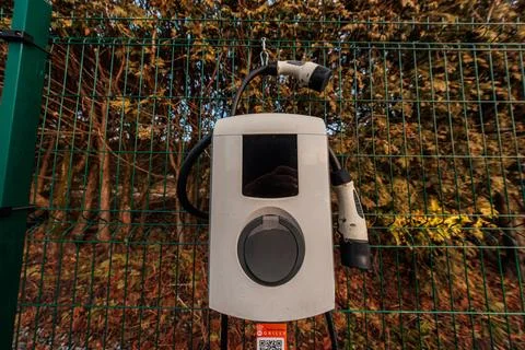 Weathered wall mounted EV charger with Type 2 connectors on fence Stock Photos