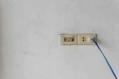 A weathered white wall featuring two old electrical outlets. 库存照片
