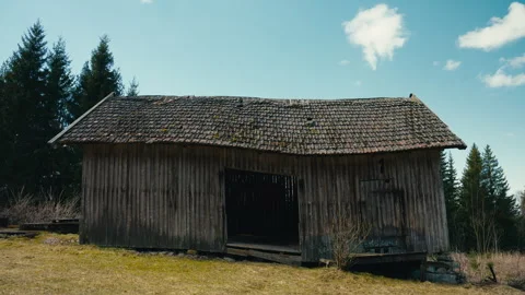 Weathered Wooden Barn Standing Alone by a Forest Under a Clear Blue Sky Stock Footage 335412953