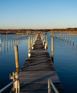 Weathered wooden dock extending into a calm tidal marsh at golden hour Stock Photos