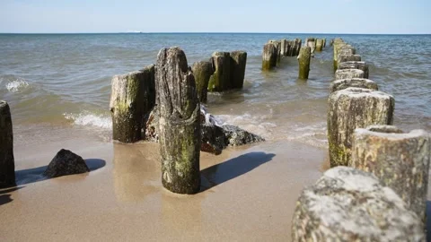 Weathered wooden posts extending into sea with gentle waves on sandy shore .. Stock Footage 333699827
