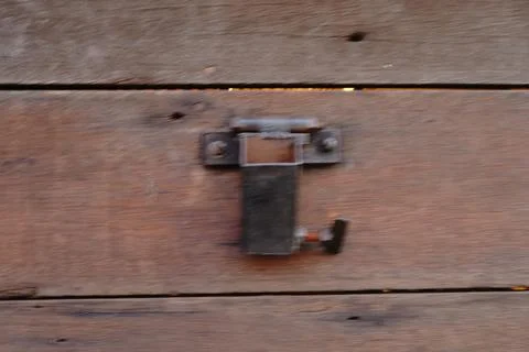 A weathered wooden surface features a rustic metal latch mechanism secured 写真素材