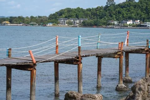 Weathered wooden walkway with rope railing extending above rocky coast in T.. Stock-Fotos