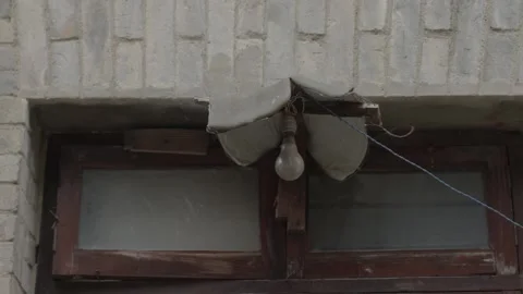 Weathered Wooden Window with Hanging Light Bulb on Gray Brick Wall Video stock 335462231