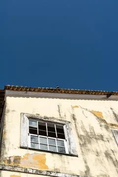 Weathered yellow facade with a broken window and a pigeon Stock Photos