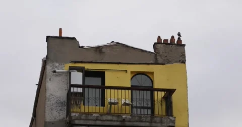 Weathered yellow rooftop balcony with crow on chimney pots Stock Footage 320172193