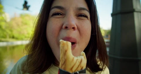 Weave active and furious happy brunette girl bites a hot dog and chews it Stock Footage 280630955