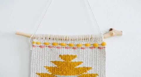 Weaved patterned piece of art ona river washed stick hanging on the wall. Stock Photos
